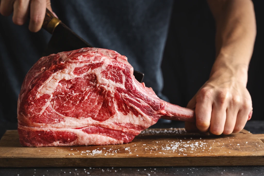 butcher-cuting-fresh-appetizing-tomahawk-steak-old-wooden-board-closeup.webp